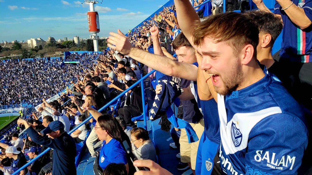 A stadium filled with spectators wearing blue jerseys, cheering and waving. 1