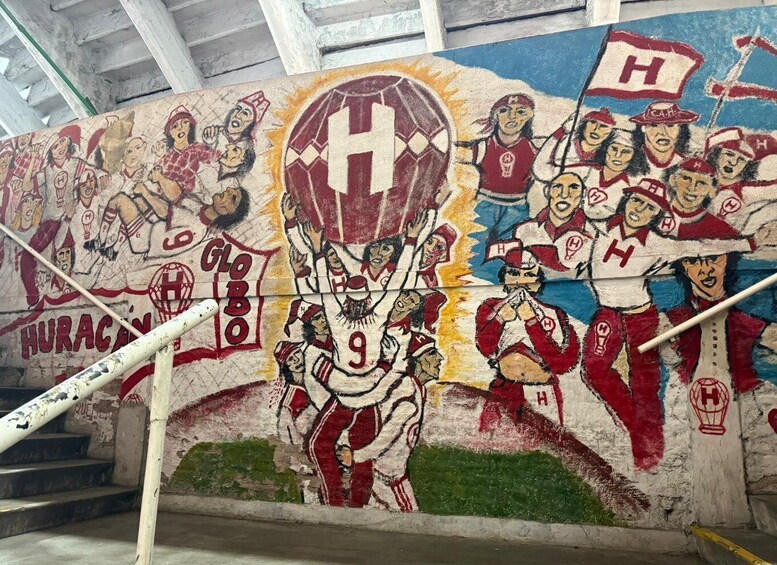 A mural of a sports team with players in red and white uniforms, a large 'H' symbol, and the word 'HURACAN' on a wall. 3