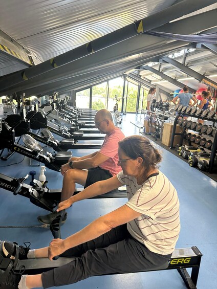People using rowing machines in a gym with weightlifting equipment and dumbbells. 5