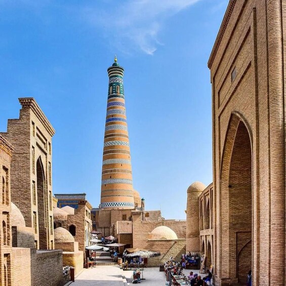 A historic tower with a spiral minaret, surrounded by traditional architecture and a bustling market area. 3