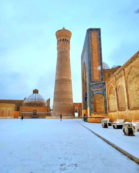 A snow-covered courtyard with a tall tower and a building with intricate tile work. 5