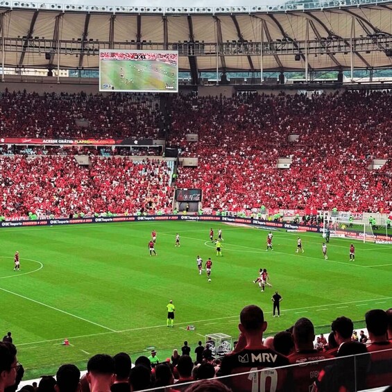 A football stadium filled with spectators, a large digital scoreboard, and players on the field. 2