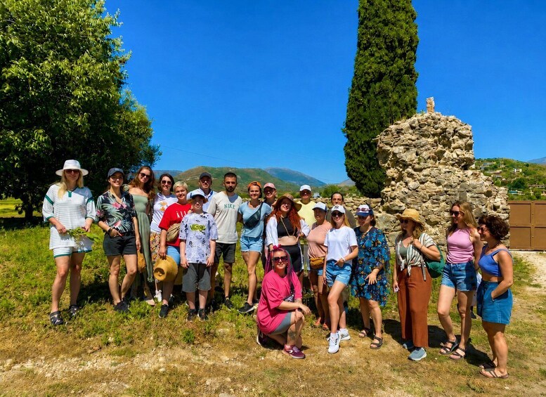 A group of people posing in a natural setting with a stone structure and trees in the background. 1