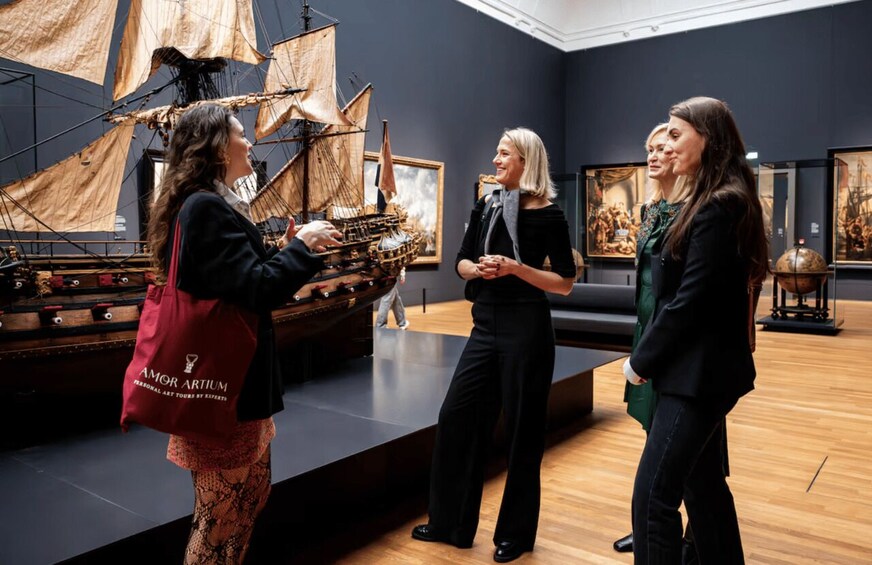 Three people in a museum with a large ship model and paintings. 4