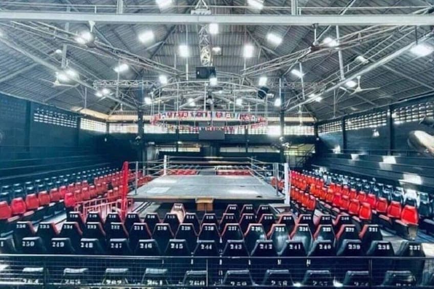 An indoor arena with red seating and a central stage. 3