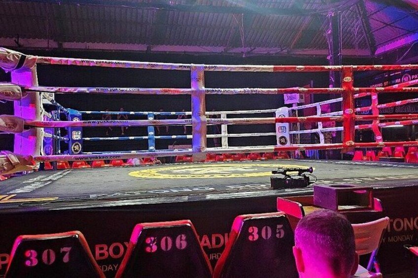A boxing ring with ropes, a referee's chair, and a boxing bag. 2