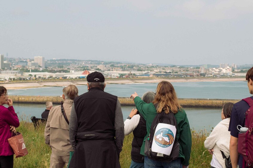 A group of people standing by a waterfront, overlooking a cityscape with buildings and a bridge. 4