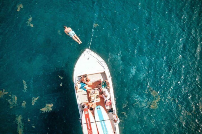 A small boat with people on board, anchored in clear blue water. 1