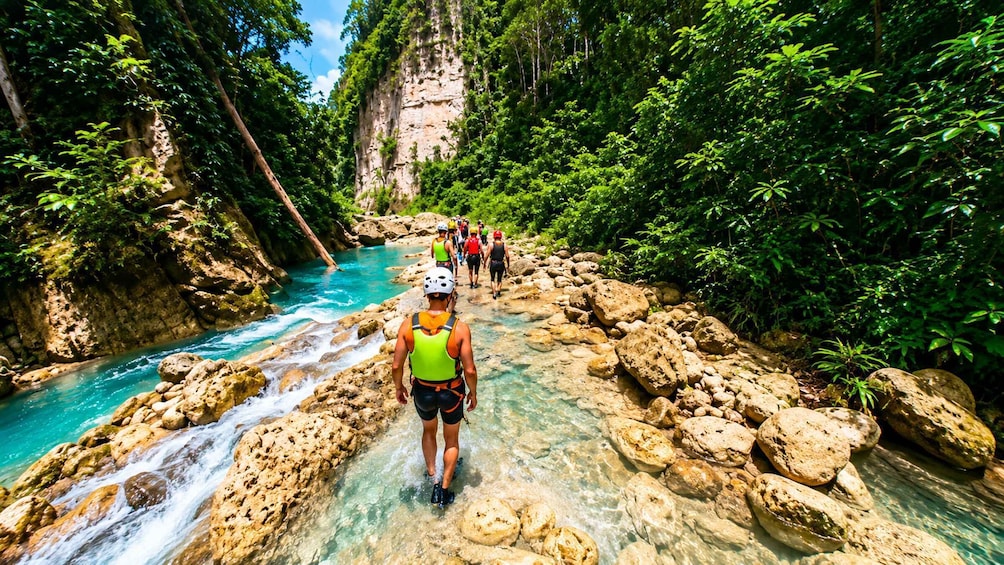 A group of hikers on a rocky riverbed surrounded by lush greenery and cliffs. 2
