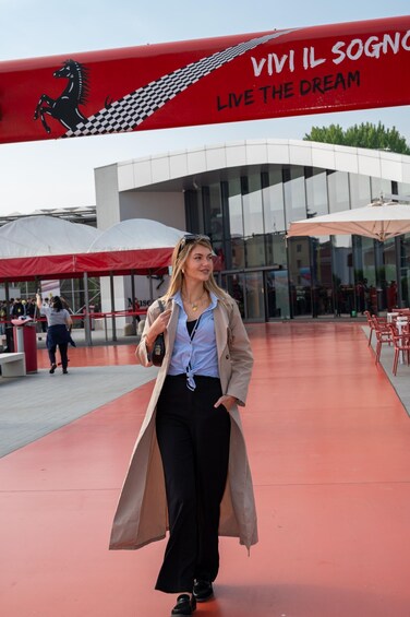 A person walking on a red carpet with a building in the background featuring a red and white checkered pattern and the text 'VIVIL SOGNO LIVE THE DREAM'. 5