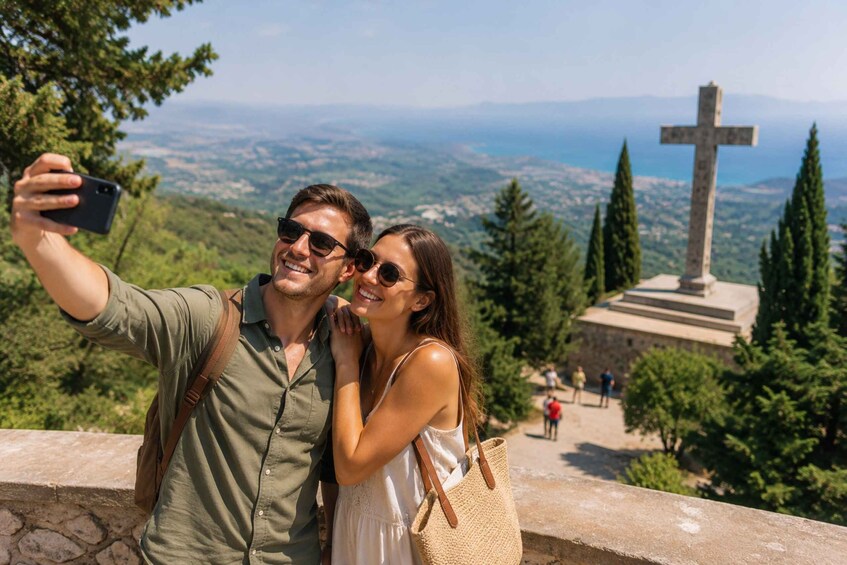 A couple taking a selfie with a cross monument and a scenic view in the background. 2