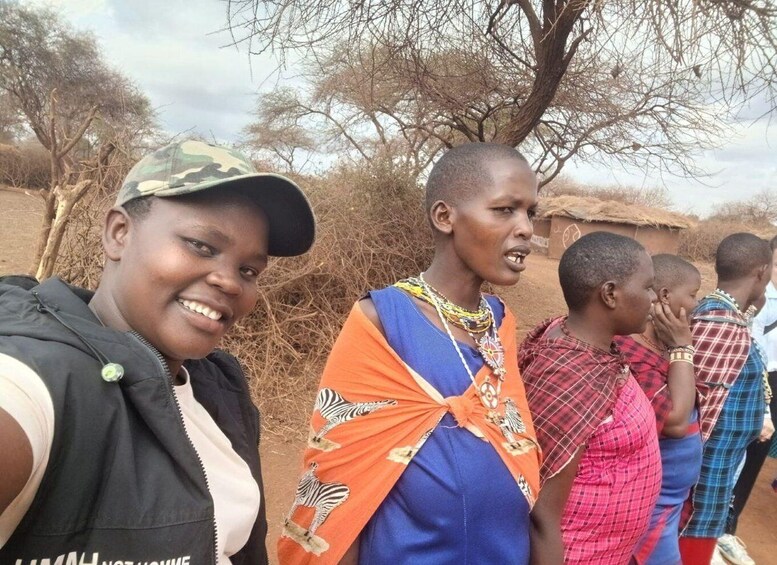A group of people outdoors with trees and a thatched-roof structure in the background. 2