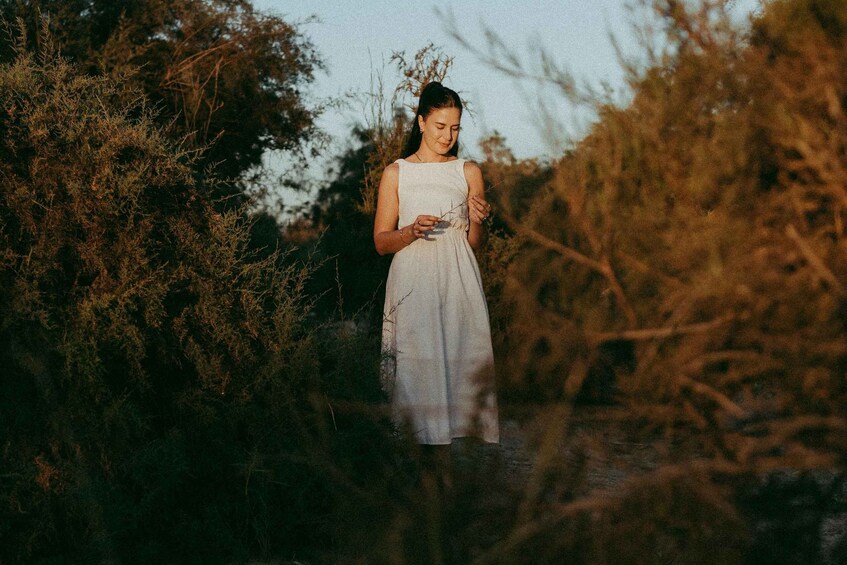 A person in a white dress standing in a natural setting with dense shrubbery. 3