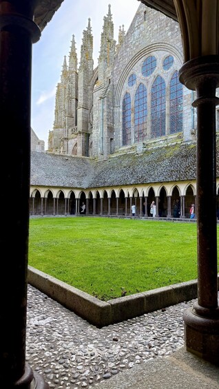 A courtyard with a green lawn, surrounded by stone columns and arches, leading to a historic cathedral with intricate spires and stained glass windows. 3