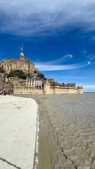 A coastal cityscape with a prominent castle-like structure, a sandy beach, and a clear blue sky. 4