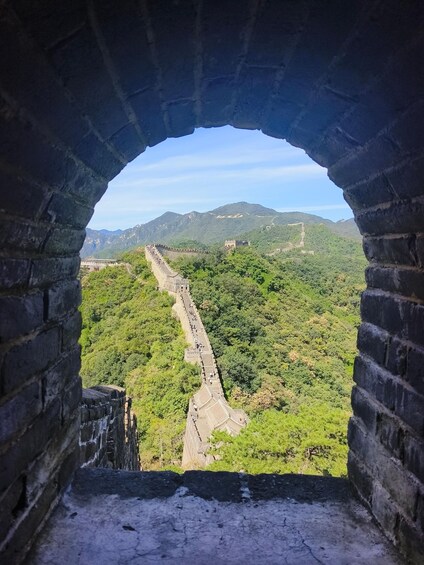 A view through a stone archway of the Great Wall of China, with lush green mountains in the background. 1