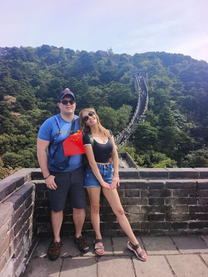 A couple standing on a stone wall overlooking a long, winding path through a forested area. 5