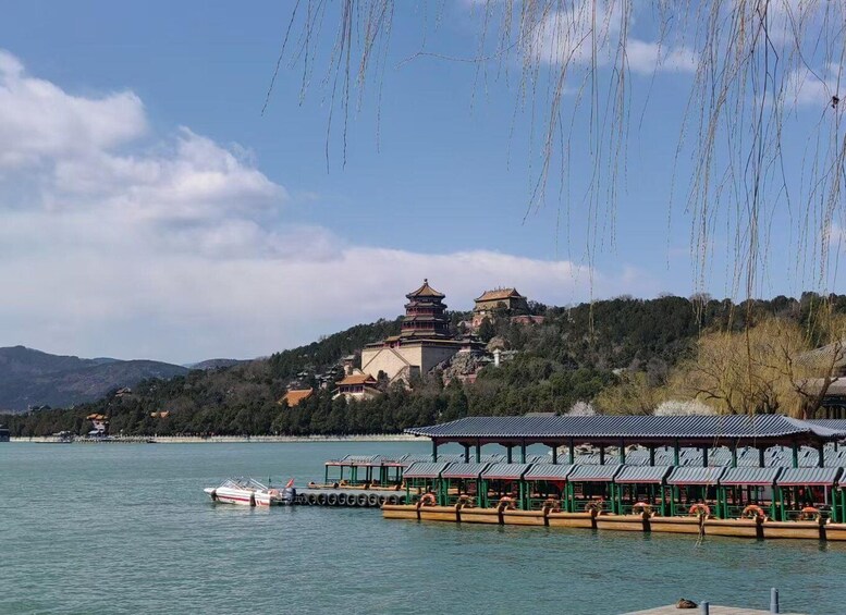 A traditional Chinese pagoda on a hill overlooking a calm lake with boats docked at a pier. 2