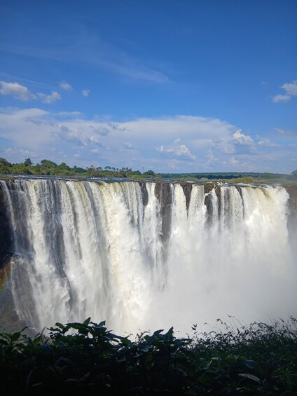 A large waterfall with multiple cascades, surrounded by lush greenery and a clear blue sky. 2
