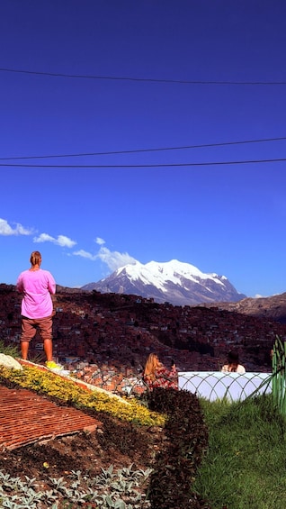 A person standing on a bridge overlooking a city with a snow-capped mountain in the background. 1