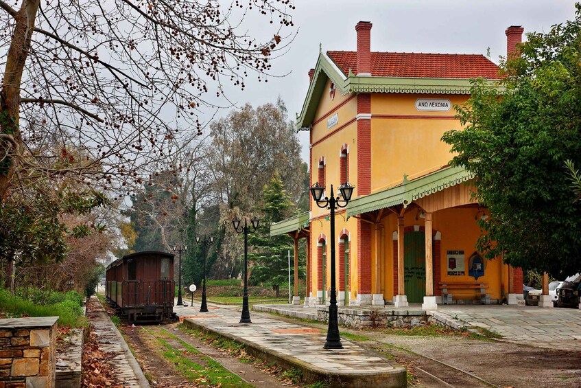 A yellow building with a red roof, a train on tracks, and trees in the background. 4
