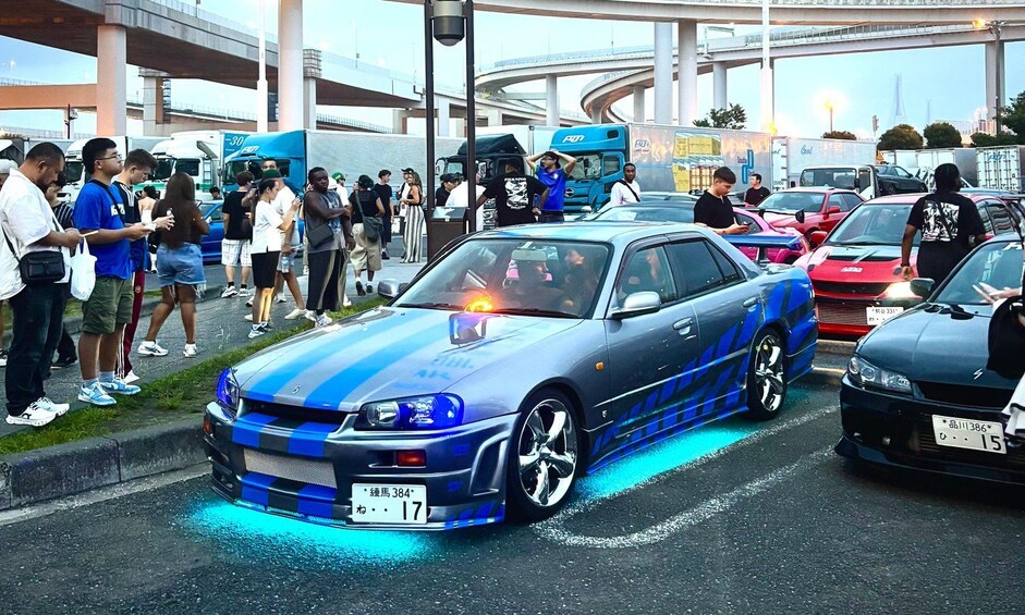 A blue sports car with blue underglow lights parked in a busy street with people and other vehicles around. 4