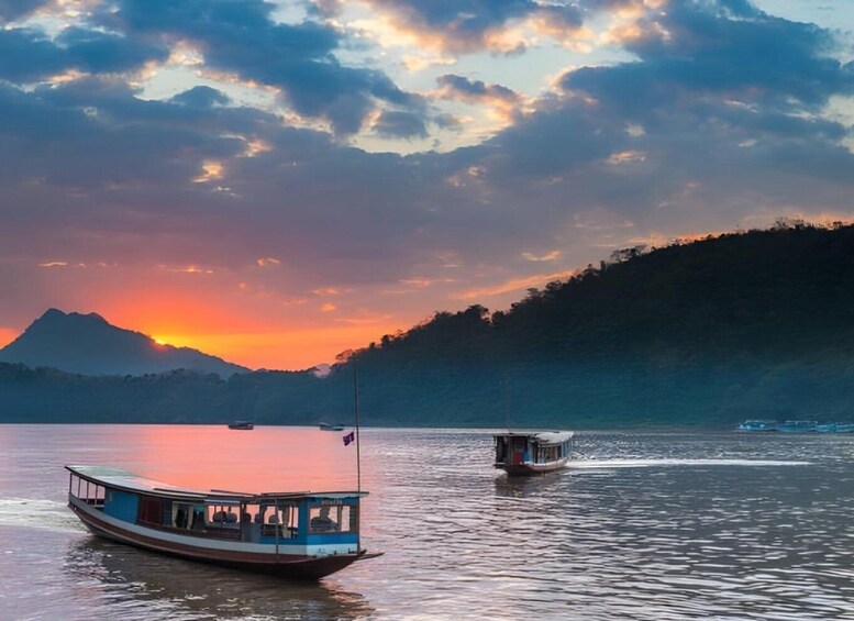A calm lake with two boats, a sunset, and a mountain in the background. 1