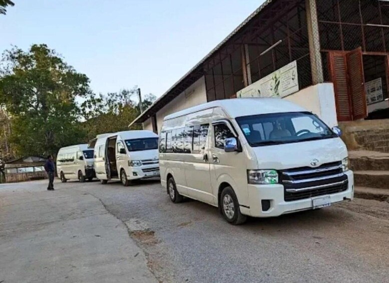 Three white vans parked in front of a building with a metal roof and a signboard. 2