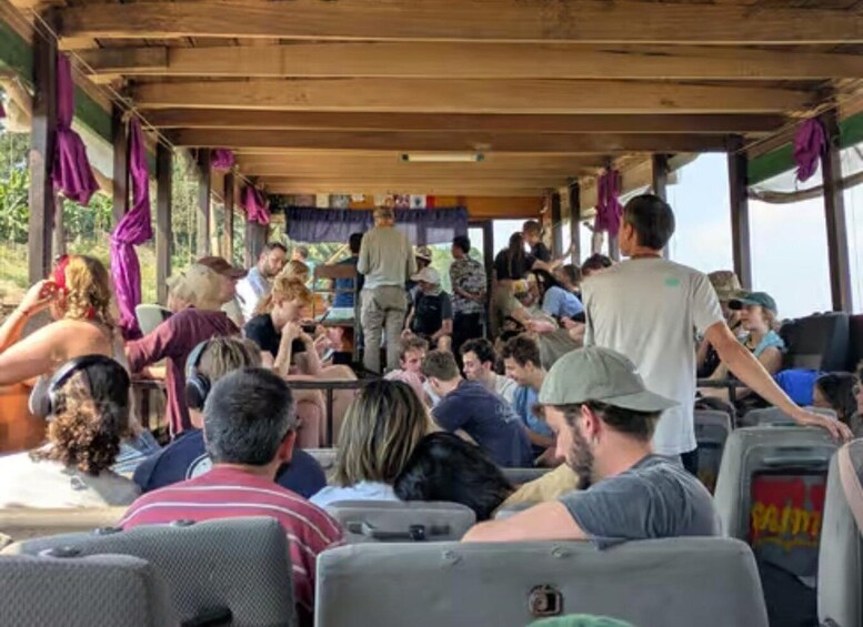 A group of people seated inside a covered bus, with some standing and others looking out. 4