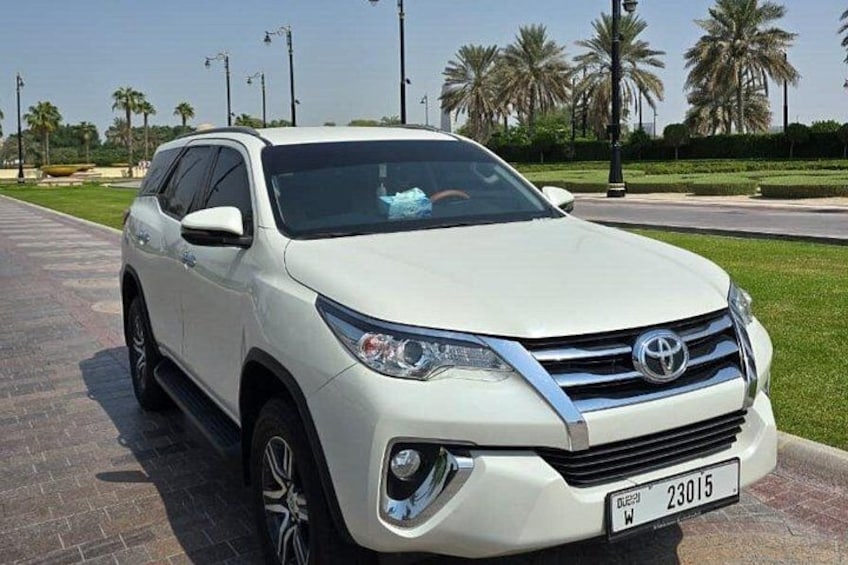 Un SUV bianco parcheggiato su una superficie asfaltata, con palme e cielo sereno sullo sfondo. 5