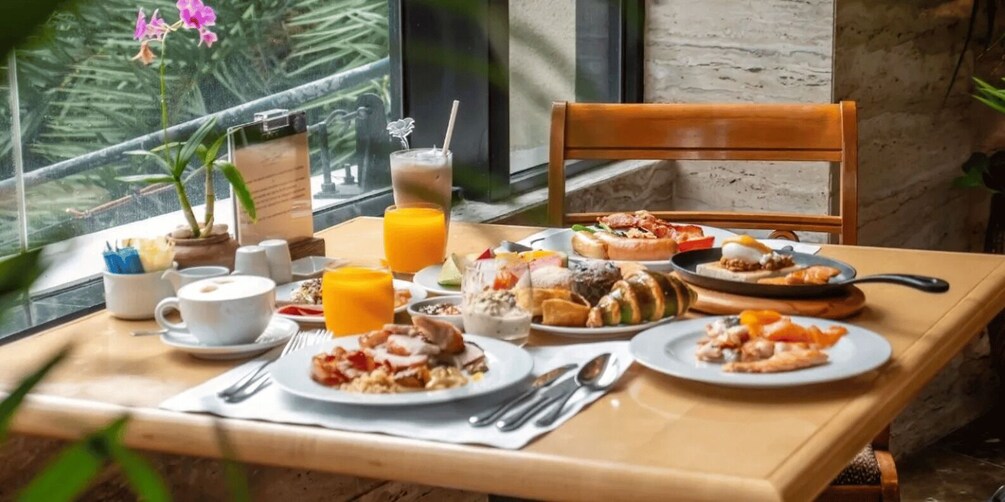 Una mesa de desayuno con diferentes platos, una taza de café y un vaso de zumo de naranja. 5