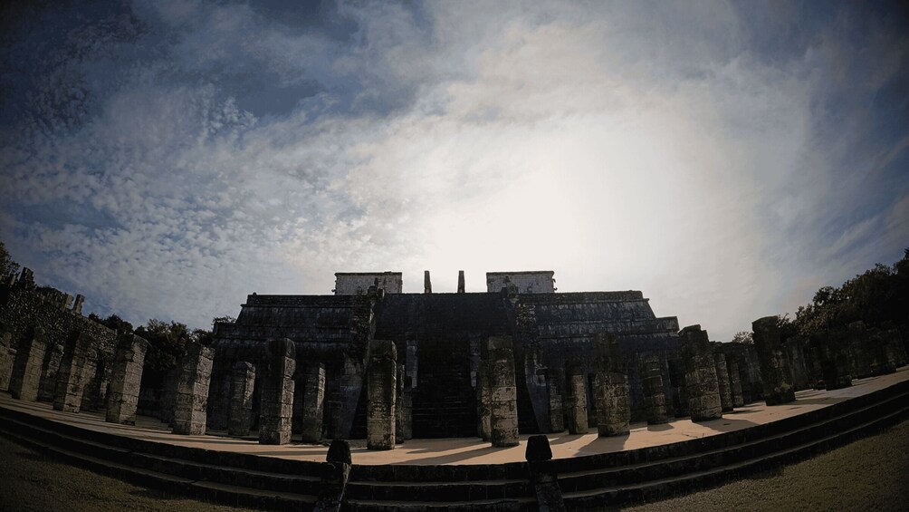 An ancient stone structure with columns and steps, under a partly cloudy sky. 2