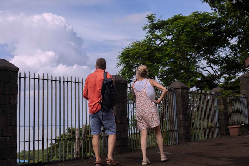 Due persone in piedi vicino a una recinzione, con vista su un ponte e alberi sullo sfondo. 4