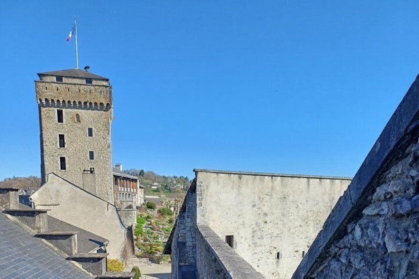 A stone tower with a flag, a building with a sloped roof, and a hillside in the background. 5