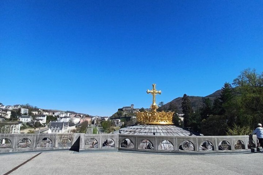 A golden cross atop a hill with a cityscape in the background. 1