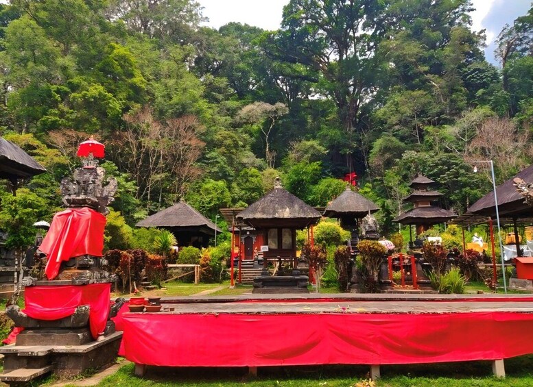 A temple complex with traditional architecture, including thatched-roof structures and stone statues, set against a backdrop of lush greenery. 2