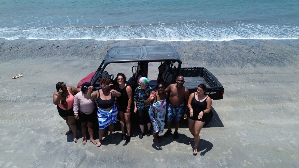 A group of people standing on a beach with a vehicle in the background. 3
