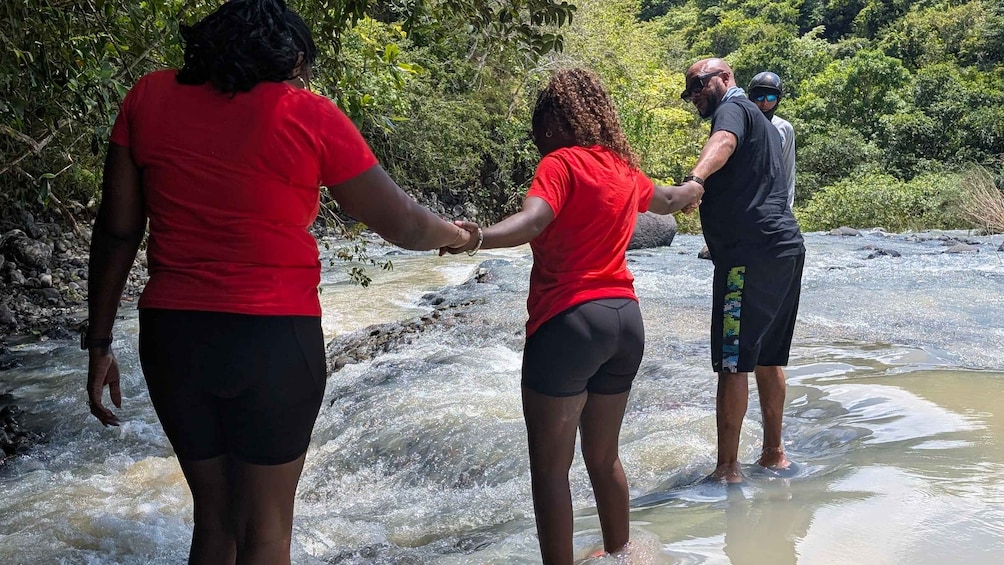 People standing in shallow water, holding hands, with a river and greenery in the background. 4