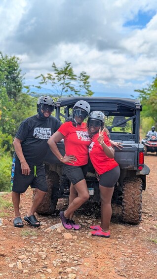Three people in red and black shirts posing with a black off-road vehicle on a dirt path. 2