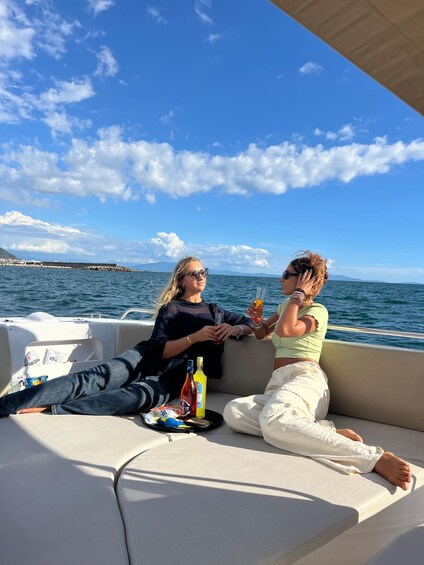 Two people sitting on a boat with drinks, overlooking a body of water and a distant shoreline. 3