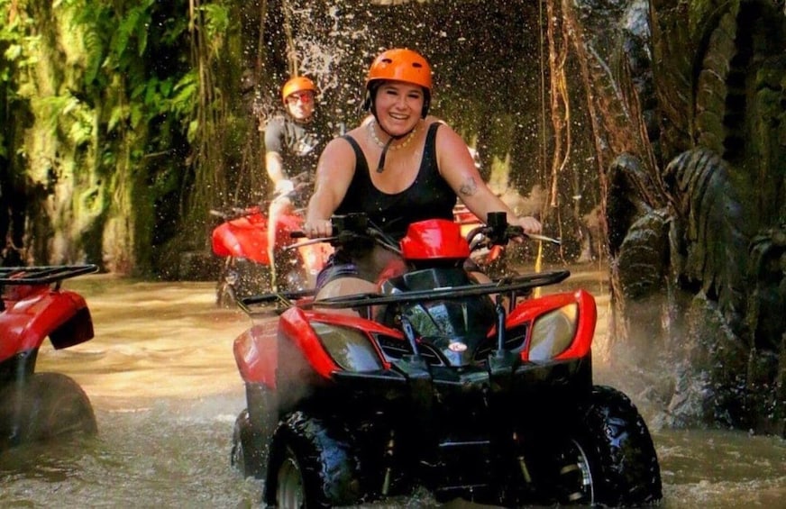 Two people on red all-terrain vehicles in a water-filled forest trail. 1
