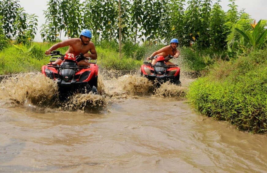 Two people riding ATVs through a muddy stream surrounded by greenery. 4