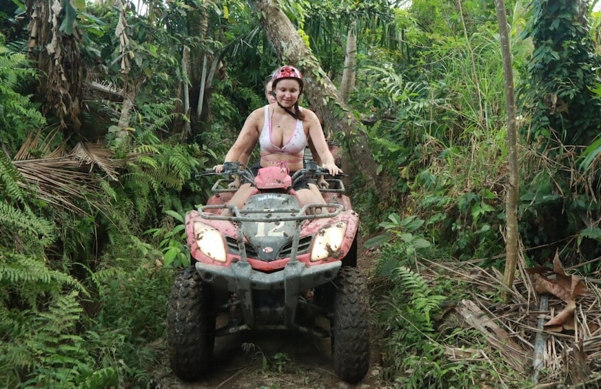 A person riding a red ATV through a dense forest. 3