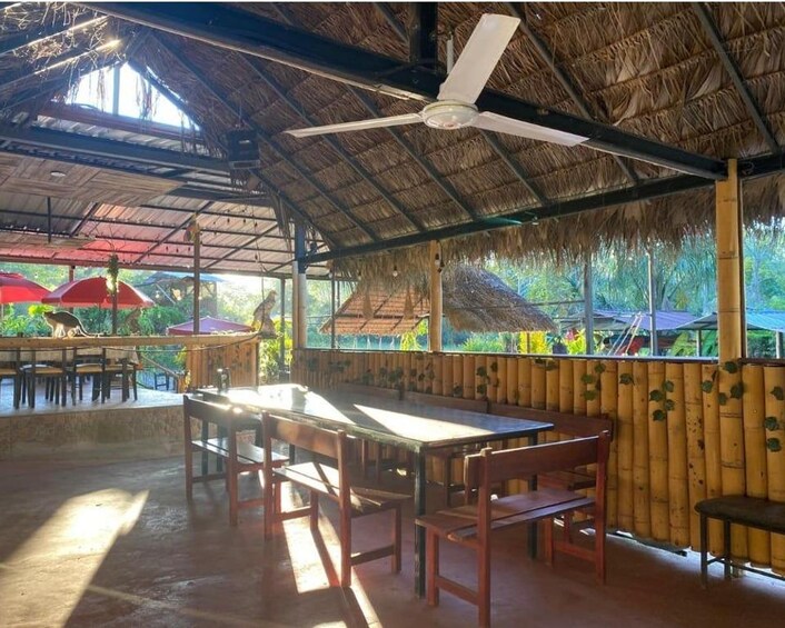 An outdoor dining area with a thatched roof, wooden tables, and chairs. 5