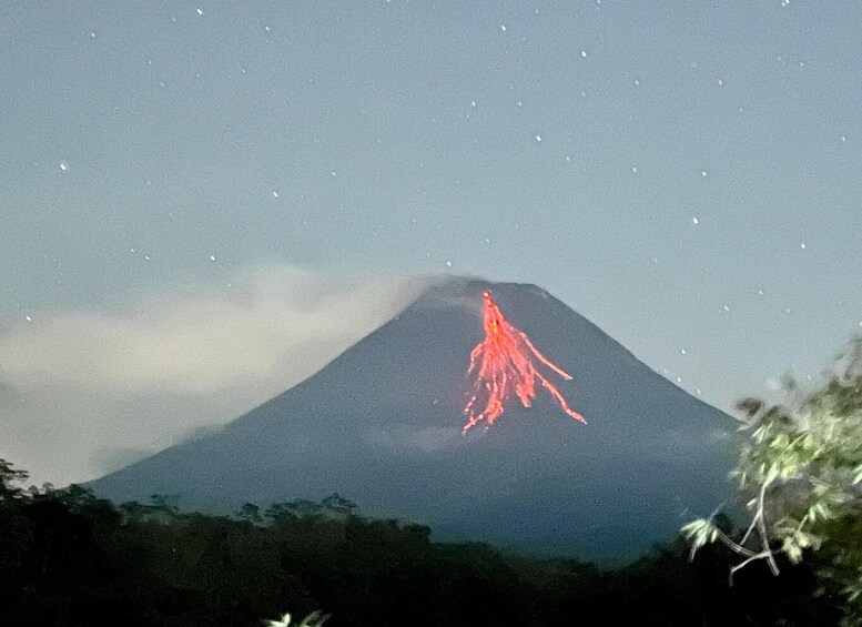 A volcano with a red glow at its peak, surrounded by clouds and vegetation. 2