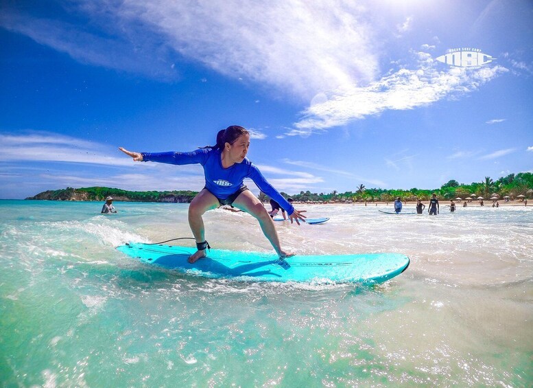 A person surfing on a clear day at a beach with other surfers and beachgoers in the background. 4