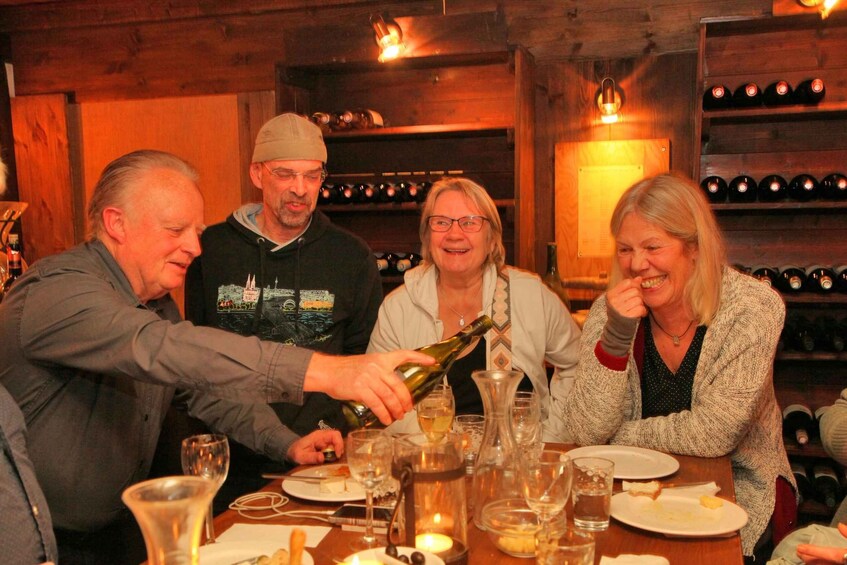 A group of people at a wooden interior setting with wine bottles on shelves. 1