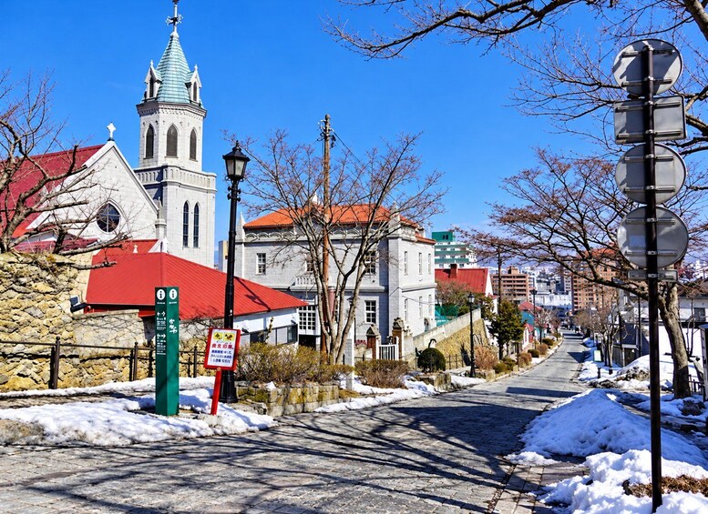 A snow-covered street with a church, a stone wall, and a signpost. 2