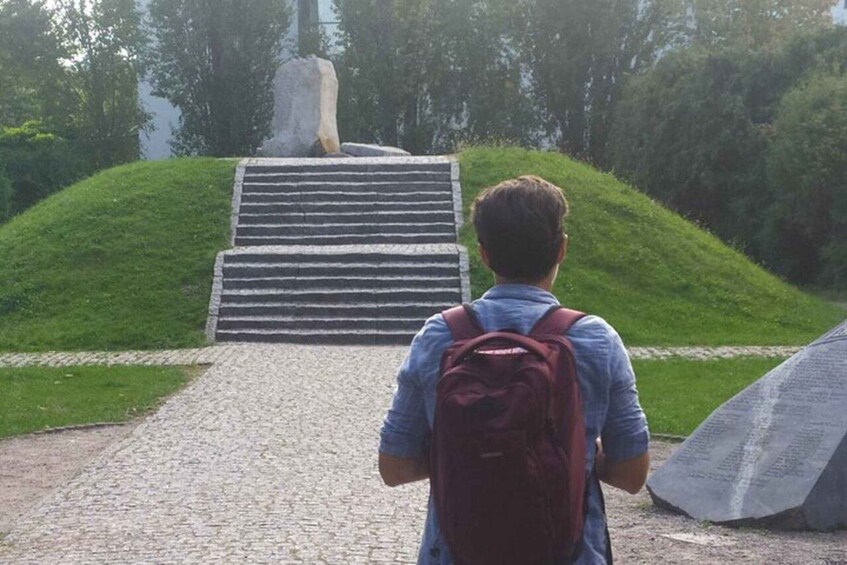 A person with a backpack walking up a stone staircase towards a monument surrounded by greenery. 3
