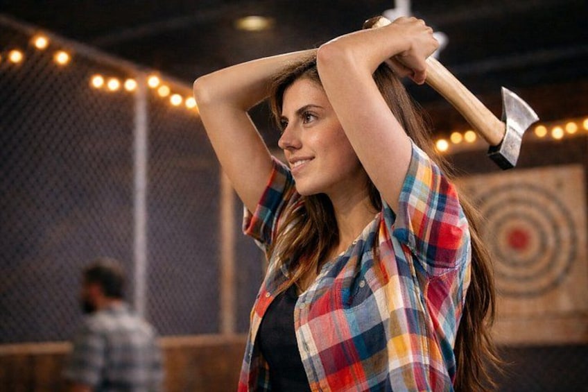 A person holding an axe, wearing a plaid shirt, in an indoor setting with a target in the background. 1